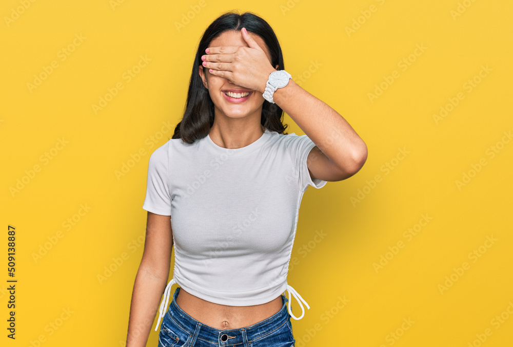 Young hispanic girl wearing casual white t shirt smiling and laughing with hand on face covering eyes for surprise. blind concept. Young hispanic girl wearing casual white t shirt smiling and laughing with hand on face covering eyes for surprise. blind concept.