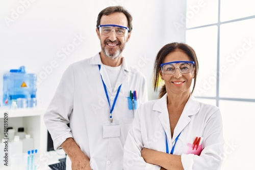 Middle age man and woman partners wearing scientist uniform standing with arms crossed gesture at laboratory