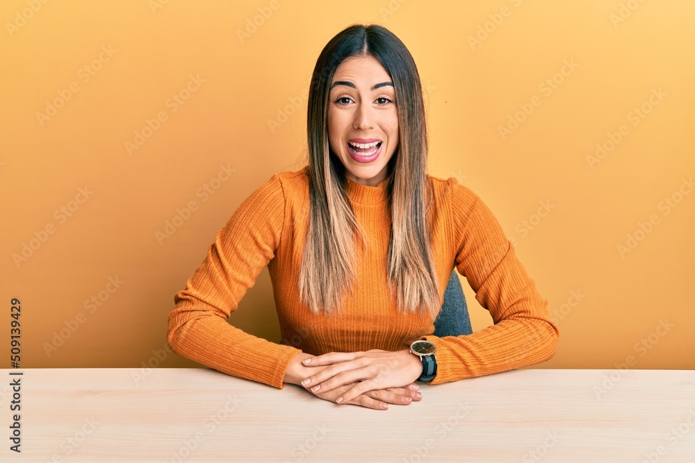 Young hispanic woman wearing casual clothes sitting on the table smiling and laughing hard out loud because funny crazy joke with hands on body. Young hispanic woman wearing casual clothes sitting on the table smiling and laughing hard out loud because funny crazy joke with hands on body.