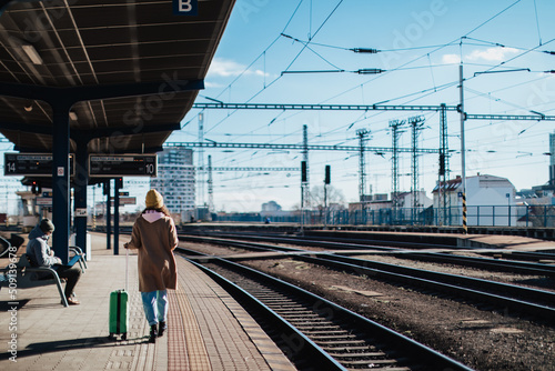 Happy young traveler woman with luggage waiting for train at train station platform photo