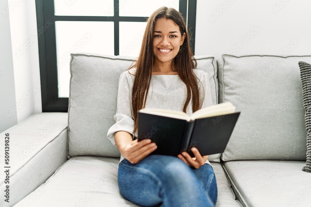 Young latin woman reading book sitting on sofa at home Young latin woman reading book sitting on sofa at home