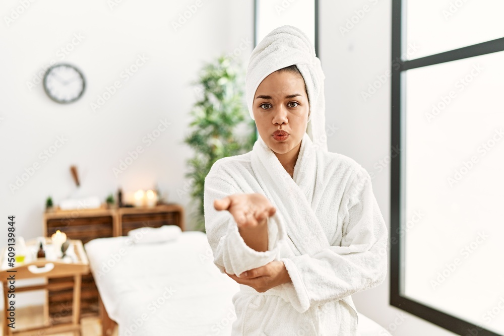 Young brunette woman wearing towel and bathrobe standing at beauty center looking at the camera blowing a kiss with hand on air being lovely and sexy. love expression. Young brunette woman wearing towel and bathrobe standing at beauty center looking at the camera blowing a kiss with hand on air being lovely and sexy. love expression.
