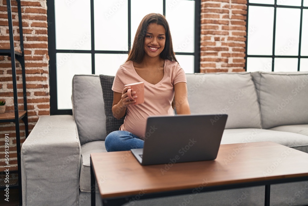 Young latin woman pregnant using laptop drinking coffee at home Young latin woman pregnant using laptop drinking coffee at home