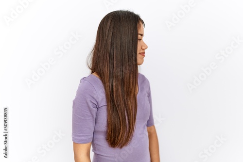 Young brunette woman standing by isolated background looking to side, relax profile pose with natural face with confident smile.