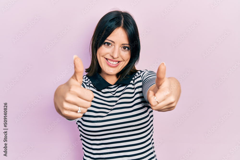Young hispanic woman wearing casual clothes approving doing positive gesture with hand, thumbs up smiling and happy for success. winner gesture.