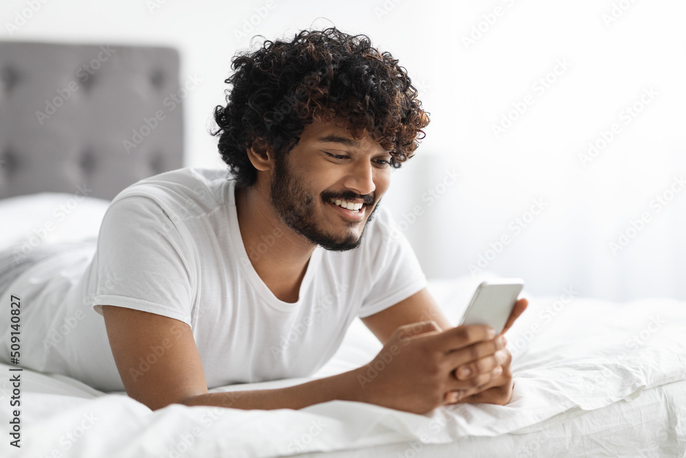 Handsome hindu guy laying on bed with phone, closeup Handsome hindu guy laying on bed with phone, closeup