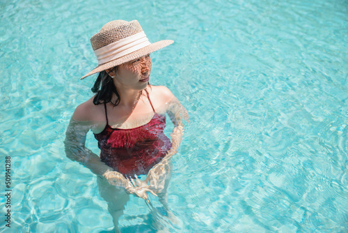 Happy asian woman in red swimsuit and a straw hat relaxing in swimming pool looking at view by the pool at Koh Mak, Phangnga, Thailand. relax and travel concept. Comfort resort summer vacation