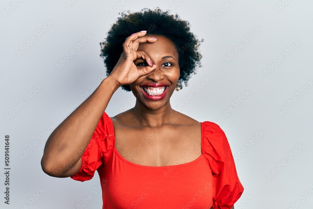 Young african american woman wearing casual clothes doing ok gesture with hand smiling, eye looking through fingers with happy face. Young african american woman wearing casual clothes doing ok gesture with hand smiling, eye looking through fingers with happy face.