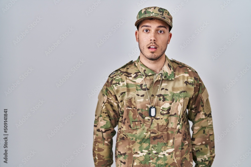 Young hispanic man wearing camouflage army uniform afraid and shocked with surprise expression, fear and excited face. Young hispanic man wearing camouflage army uniform afraid and shocked with surprise expression, fear and excited face.