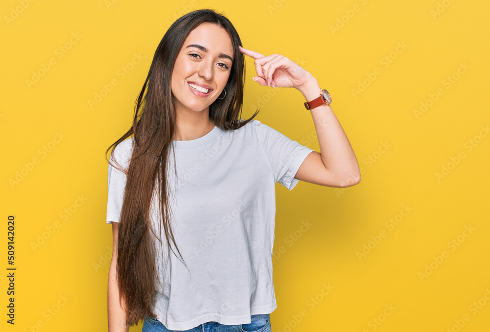 Young hispanic girl wearing casual white t shirt smiling pointing to head with one finger, great idea or thought, good memory Young hispanic girl wearing casual white t shirt smiling pointing to head with one finger, great idea or thought, good memory
