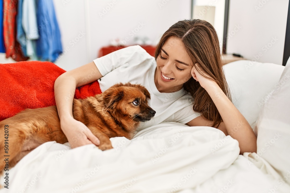 Young hispanic woman hugging dog lying on bed at bedroom Young hispanic woman hugging dog lying on bed at bedroom