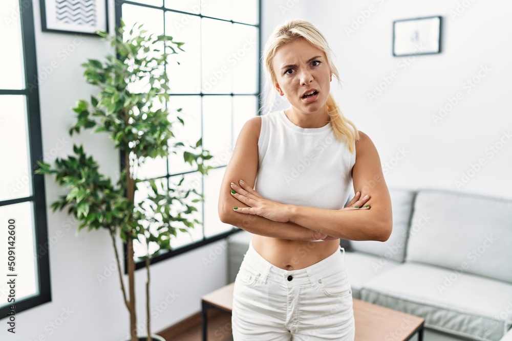 Young caucasian woman standing at living room skeptic and nervous, disapproving expression on face with crossed arms. negative person. Young caucasian woman standing at living room skeptic and nervous, disapproving expression on face with crossed arms. negative person.