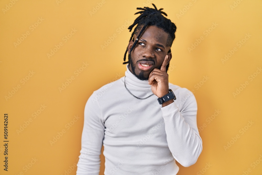 African man with dreadlocks wearing turtleneck sweater over yellow background thinking worried about a question, concerned and nervous with hand on chin African man with dreadlocks wearing turtleneck sweater over yellow background thinking worried about a question, concerned and nervous with hand on chin