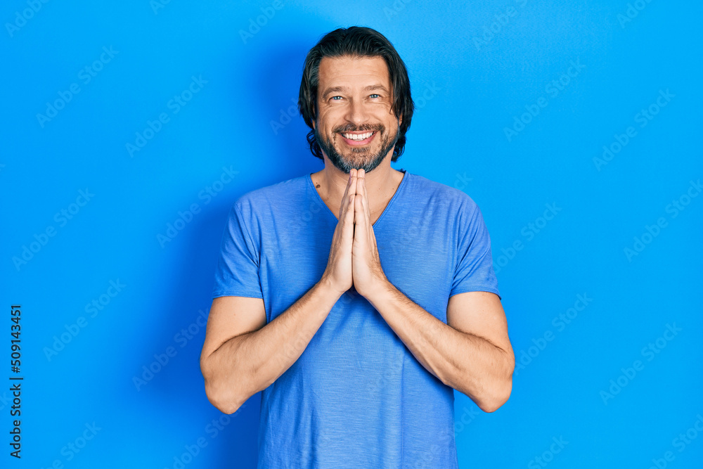 Middle age caucasian man wearing casual clothes praying with hands together asking for forgiveness smiling confident.