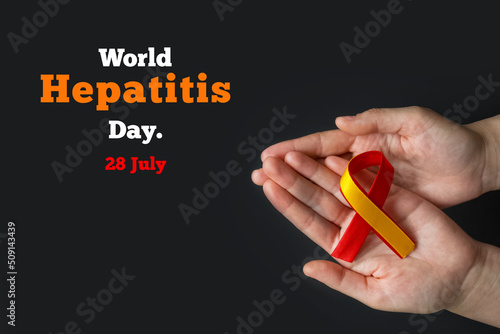 World hepatitis day. Adult hands holding red yellow ribbon on black background. Awareness of prevention and treatment viral hepatitis. Liver cancer. World cancer day. copy space. banner