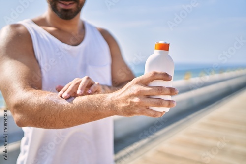 Hispanic sports man wearing workout style applying sunscreen on arm outdoors on a sunny day