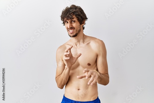 Young hispanic man standing shirtless over isolated, background disgusted expression, displeased and fearful doing disgust face because aversion reaction. with hands raised