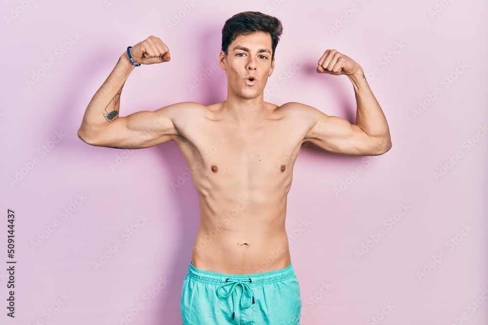 Young hispanic man wearing swimwear shirtless showing arms muscles smiling proud. fitness concept.