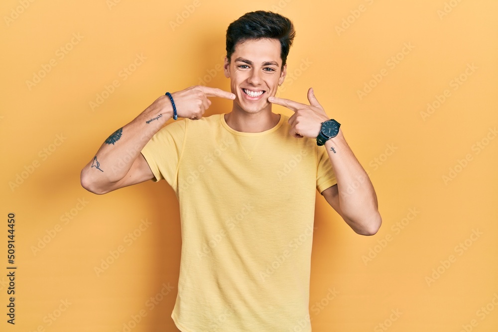 Young hispanic man wearing casual yellow t shirt smiling cheerful showing and pointing with fingers teeth and mouth. dental health concept. Young hispanic man wearing casual yellow t shirt smiling cheerful showing and pointing with fingers teeth and mouth. dental health concept.