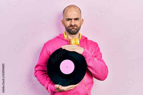 Young bald man holding vinyl disc skeptic and nervous, frowning upset because of problem. negative person.