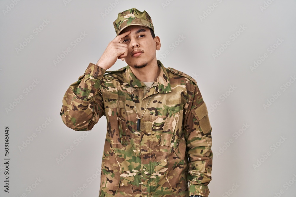 Young arab man wearing camouflage army uniform pointing unhappy to pimple on forehead, ugly infection of blackhead. acne and skin problem Young arab man wearing camouflage army uniform pointing unhappy to pimple on forehead, ugly infection of blackhead. acne and skin problem