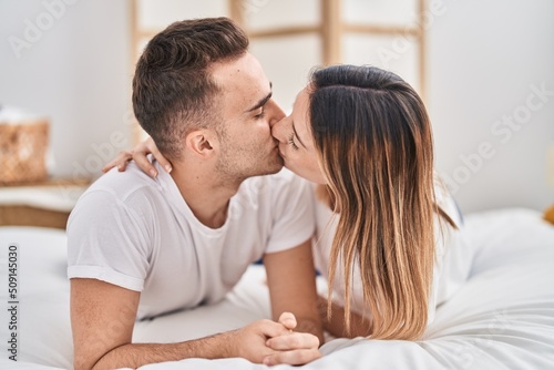 Man and woman couple lying on bed hugging each other and kissing at bedroom