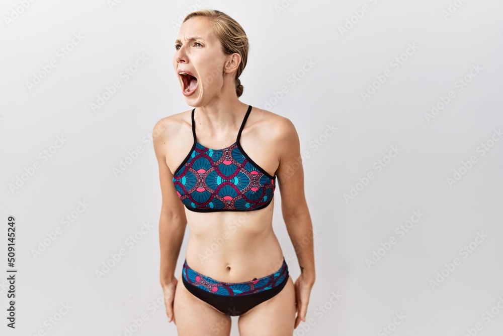 Naklejka premium Young blonde woman wearing sporty bikini over isolated background angry and mad screaming frustrated and furious, shouting with anger. rage and aggressive concept.
