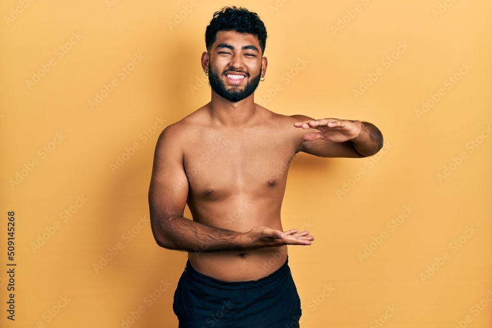 Arab man with beard wearing swimwear shirtless gesturing with hands showing big and large size sign, measure symbol. smiling looking at the camera. measuring concept. Arab man with beard wearing swimwear shirtless gesturing with hands showing big and large size sign, measure symbol. smiling looking at the camera. measuring concept.