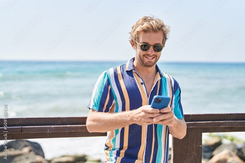 Young man tourist smiling confident using smartphone at seaside