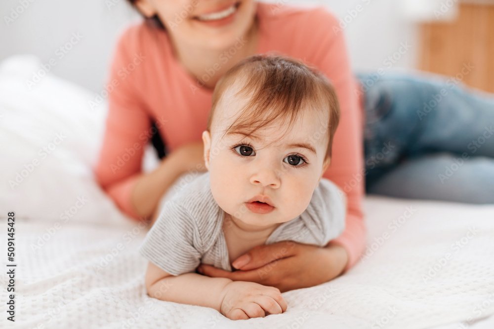 Closeup portrait of cute little kid, mom helping her crawl on bed in bedroom at home Closeup portrait of cute little kid, mom helping her crawl on bed in bedroom at home
