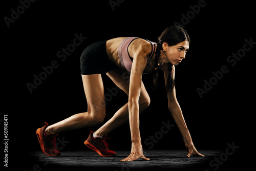Ready to start. Studio shot of young muscular woman running isolated on black background. Sport, track-and-field athletics, competition and active lifestyle concept