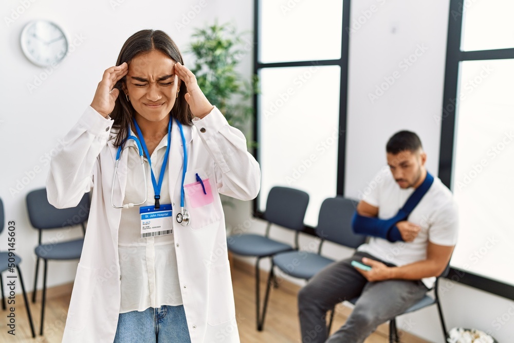 Fototapeta premium Young asian doctor woman at waiting room with a man with a broken arm with hand on head for pain in head because stress. suffering migraine.