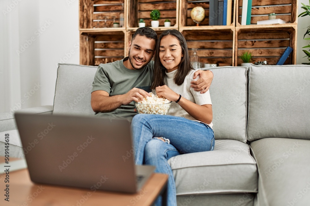 Young hispanic couple watching film and eating popcorn sitting on the sofa  at home. foto de Stock | Adobe Stock