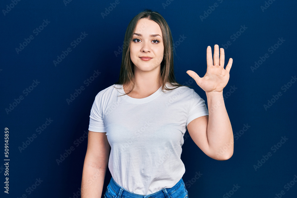Fototapeta premium Young hispanic girl wearing casual white t shirt showing and pointing up with fingers number five while smiling confident and happy.