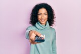 Young latin girl holding television remote control looking positive and happy standing and smiling with a confident smile showing teeth
