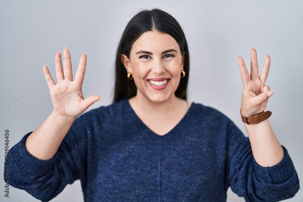 Young brunette woman standing over isolated background showing and pointing up with fingers number eight while smiling confident and happy. Young brunette woman standing over isolated background showing and pointing up with fingers number eight while smiling confident and happy.