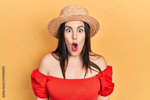 Young hispanic woman wearing summer hat afraid and shocked with surprise expression, fear and excited face.
