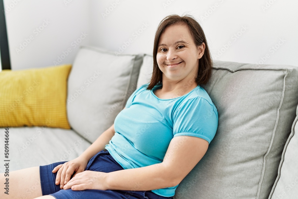 Brunette woman with down syndrome sitting on the sofa at the living room Brunette woman with down syndrome sitting on the sofa at the living room