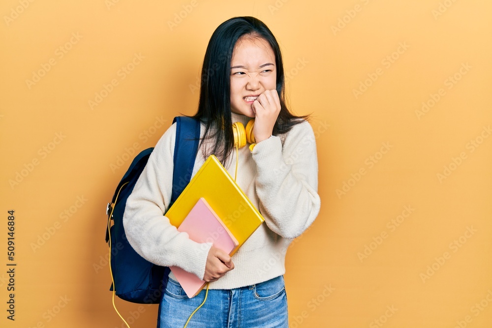 Young chinese girl holding student backpack and books looking stressed and nervous with hands on mouth biting nails. anxiety problem. Young chinese girl holding student backpack and books looking stressed and nervous with hands on mouth biting nails. anxiety problem.