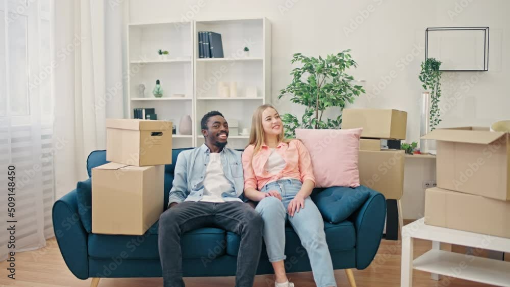 Young happy couple sitting on sofa of a nice new apartment, moving in together Young happy couple sitting on sofa of a nice new apartment, moving in together