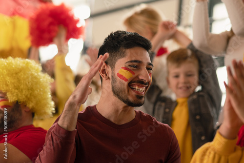 Excited, happy football fans supproting spanish national team in live soccer match at stadium.
