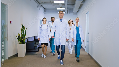 Big team of doctors and nurses multiethnic in the hospital corridor walking in front of the camera straight