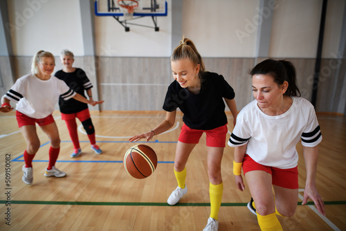 Young and senior women playing basketball match in gym. © Halfpoint