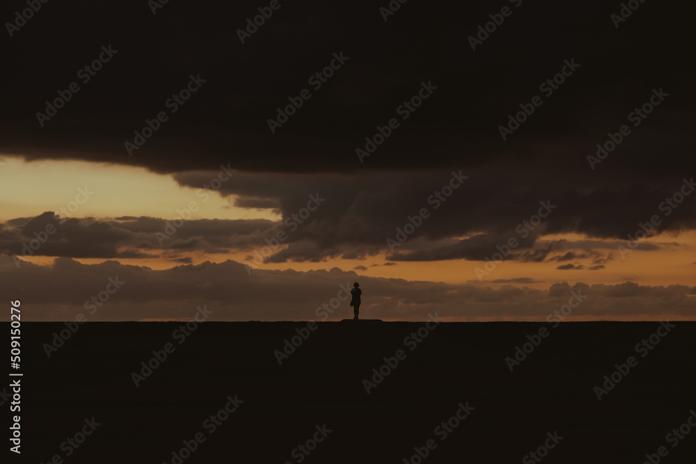 silhouette of a female traveler in a beautiful cloudy sunset on the beach, at the golden hour