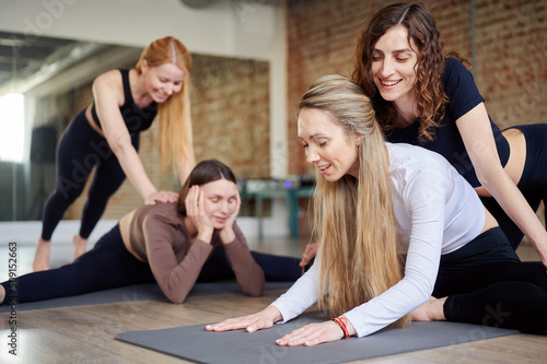 Yoga class in fitness studio. Girls stretching lesson with instructor indoors on yoga mat. Fitness, sport, training, gym and lifestyle concept