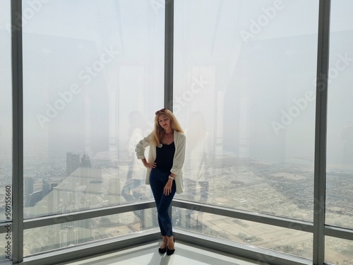 Print op canvas Beautiful girl stands by the window of skyscraper with an amazing panoramic view over the Dubai city and fountains from Burj Khalifa, United Arab Emirates