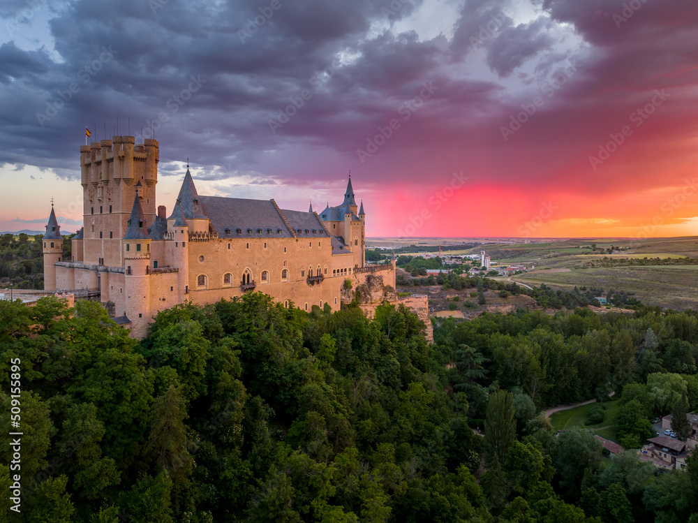 Sunset over the Alcázar of Segovia medieval castle in Castile and León, Spain. Rising out on a rocky crag above the confluence of two rivers with majestic red, orange, yellow as the sun paints the sky