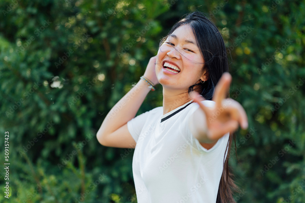 Young Caucasian asian woman making the peace sign outdoors