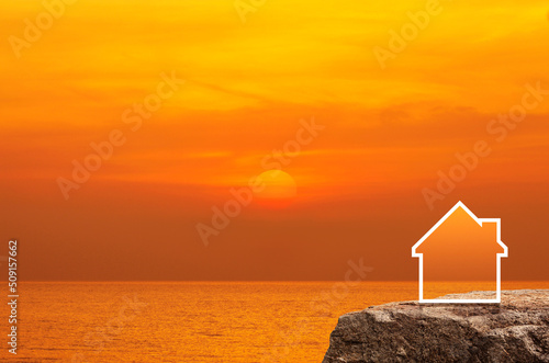 House icon with copy space on rock mountain over sunset sky and sea, Business real estate concept