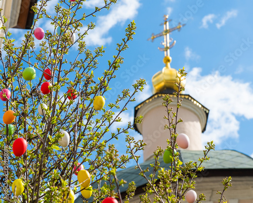 Fotografia Colorful easter eggs on the tree near the church in sunny spring